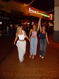 three women are walking down the street holding their arms in the air and one has her hand up