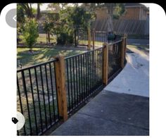 an iron fence with wood posts and gated in area next to the sidewalk,