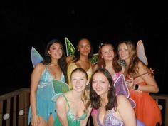 a group of women dressed in fairy costumes posing for a photo on a deck at night