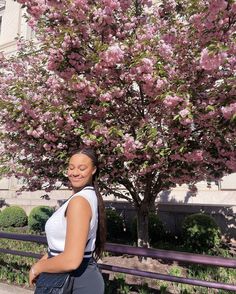 a woman standing in front of a tree with pink flowers