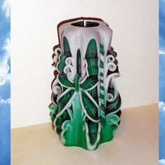 a green and white vase sitting on top of a table next to a cloud filled sky