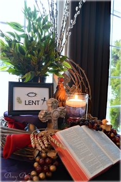 an open book sitting on top of a table next to a candle and some plants