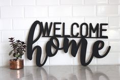 a metal sign that says welcome home next to a potted plant on a counter