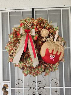 a wreath on the front door with two apples hanging from it's sides and ribbons