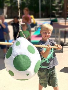 a young boy holding onto a large green and white ball hanging from a wooden pole