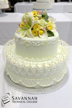 two tiered wedding cake with flowers on top and white lace around the edges, sitting on a table