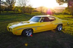 a yellow muscle car parked in the grass with the sun shining on it's side