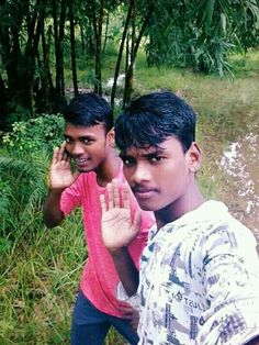 two young men standing next to each other in front of some trees and grass with their hands up