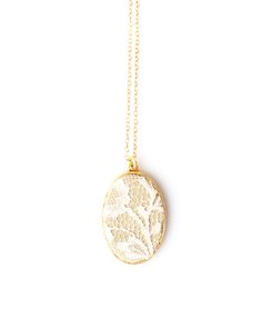 a gold necklace with a white lace on the front and an oval pendant hanging from it