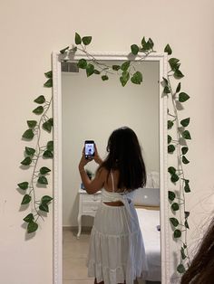 a woman taking a selfie in front of a mirror with ivy growing on it