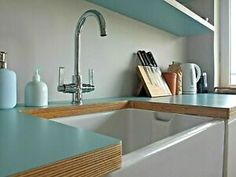 a kitchen sink with blue counter tops and wooden shelves in the corner next to it