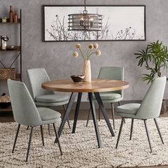 a dining room table with four chairs and a vase on top of it in front of a gray wall