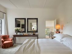 a bed with white sheets and pillows in a bedroom next to two mirrors on the wall