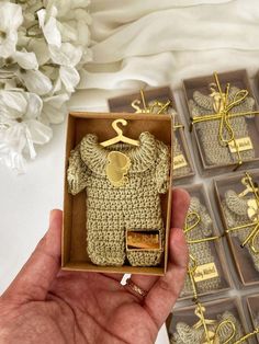 someone is holding up a tiny crocheted baby sweater in a box with tags on it