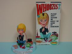 a toy doll sitting on top of a table next to a box of whioozies