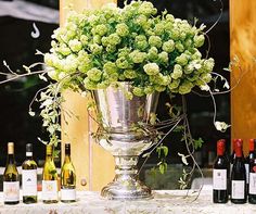 a silver vase filled with green flowers next to bottles of wine