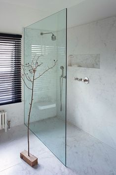 a bathroom with a glass shower door and white marble walls, along with a bare tree branch in the corner