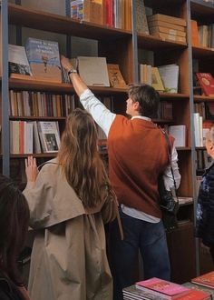 people are looking at books on shelves in a library with one person reaching up for the book