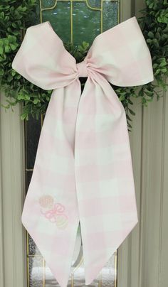 a pink and white bow hangs on the front door with greenery in the background