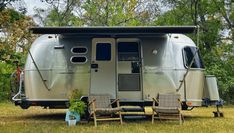 an rv parked in the grass with two lawn chairs and a potted plant next to it