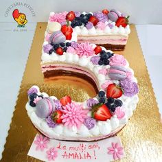 a cake shaped like the number five with flowers and fruits on it, sitting on a table