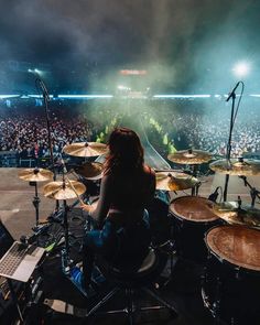 a woman sitting on top of a drum set in front of a crowd at a concert