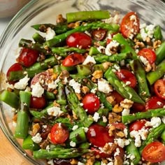 a glass bowl filled with asparagus, cherry tomatoes and feta cheese on top