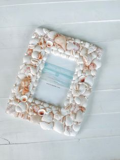 a frame made out of seashells on a white wooden surface with the words sea shore written in it