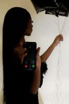 a woman holding a cell phone in front of a wall with balloons attached to it