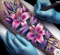 a tattoo artist working on a woman's arm with purple flowers and dragonflies