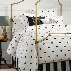 a bed with black and white hearts on it, next to a nightstand with a lamp