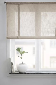 a white vase with a plant in it sitting on a window sill next to a window