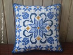 a blue and white cross stitch pillow sitting on top of a wooden table