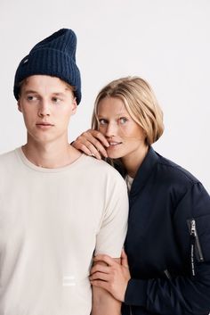 two people standing next to each other in front of a white background, one wearing a blue hat