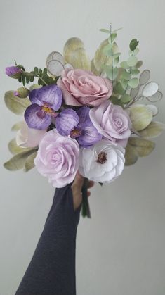 a person holding a bouquet of flowers in their hand with white, pink and purple flowers