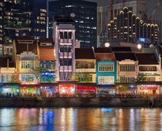 the city skyline is lit up at night with brightly colored buildings and lights reflecting in the water