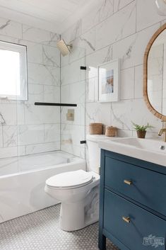 a white toilet sitting next to a bath tub under a bathroom mirror on top of a wooden cabinet