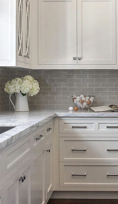 a kitchen with white cabinets and marble counter tops