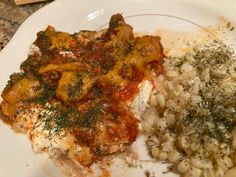 a white plate topped with pasta and meat covered in marinara sauce next to rice