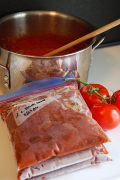 some tomatoes and meat in a bag on a table next to a pot with a wooden spoon