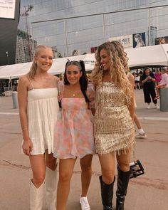 three young women standing next to each other in front of a tall building with glass windows