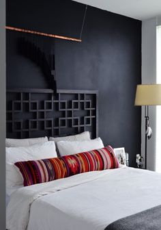 a bedroom with black walls, white bedding and colorful pillows on the headboard