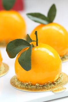 there are three oranges with leaves on top of each one, sitting on gold plates