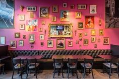 a restaurant with pink walls, black leather booths and pictures on the wall above them