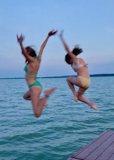 two women jumping into the air from a dock in front of blue water and sky