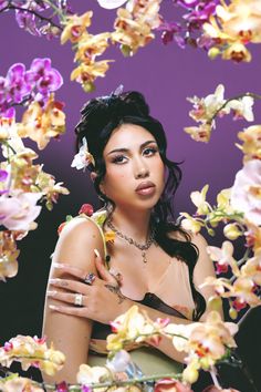 a woman with flowers in her hair and ring on her finger, surrounded by orchids