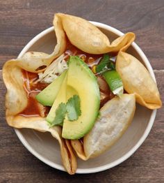 a white bowl filled with tortilla shells covered in sauce and avocado