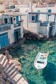 a woman standing on the steps leading to a boat in clear blue water near buildings