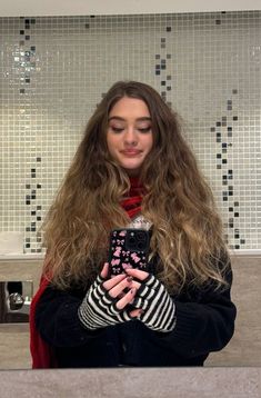 a woman with long hair is looking at her cell phone while standing in the bathroom