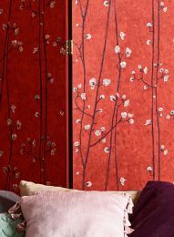 a bed sitting next to a red wall with flowers on the walls and pillows in front of it